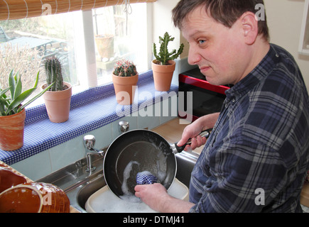 Man washing up pots with little enthusiam at a kitchen sink at home ...