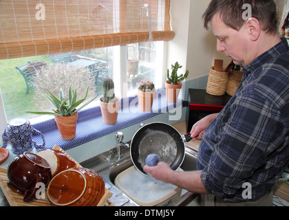 Man washing up pots with little enthusiam at a kitchen sink at home ...