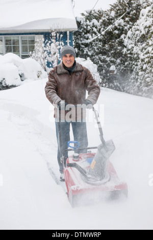 Man using snowblower to clear deep snow on driveway near residential house after heavy snowfall. Stock Photo