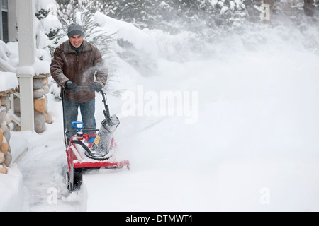 Man using snowblower to clear deep snow on driveway near residential house after heavy snowfall. Stock Photo