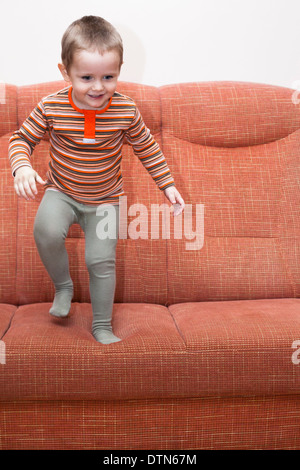 Happy playful child boy jumping on sofa. Stock Photo