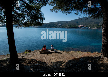 A couple enjoy the view across the bay to the artist's town of Cadaques, Cap de Creus peninsula, Costa Brava, Catalonia, Spain Stock Photo