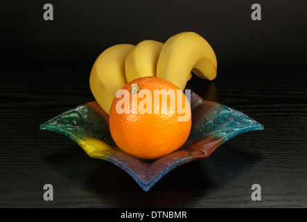 Bananas and orange in colored glass bowl Stock Photo