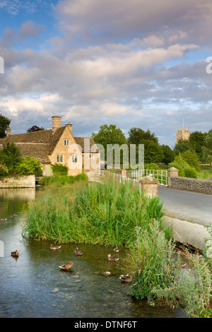 Evening sunlight glows on the old mill and church in the Cotswolds village of Fairford, Gloucestershire, England. Stock Photo