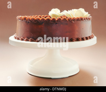 All chocolate birthday cake, on brown background, decorated with yellow flowers on top. Stock Photo