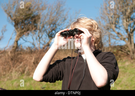 White, blond teenage boy looking through binoculars on a sunny day in the English countryside birdspotting Stock Photo