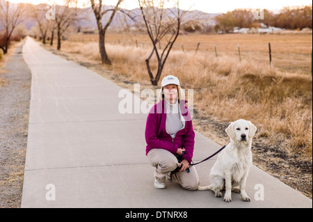 Woman walking six month old platinum golden retriever dog on bike path at sunset, small mountain town of Salida, Colorado, USA Stock Photo