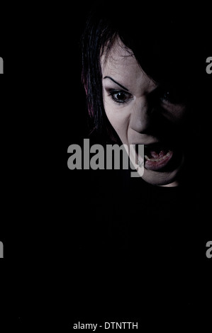 Angry man screaming, shouting, a dark scary headshot, moody portrait taken against black background Stock Photo