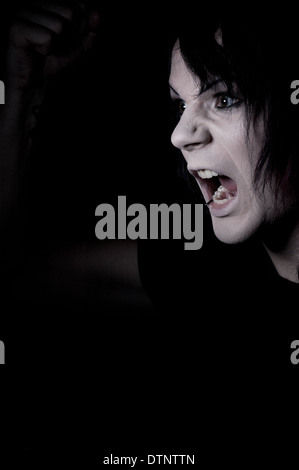 man screaming with anger, a moody portrait concept taken against black background Stock Photo