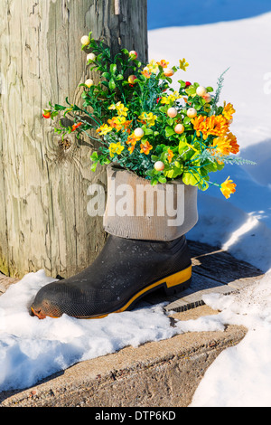 Silk flower in a rubber boot amongst the snow. Stock Photo