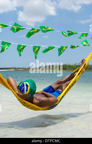 Man relaxing in hammock over the sea with Brazilian flag bunting Stock Photo