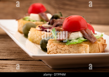 Crostini with mozzarella cheese anchovy and tomato on wooden board Stock Photo
