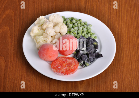 heap of frozen tomato, asparagus, peas and cauliflower on the white plate Stock Photo