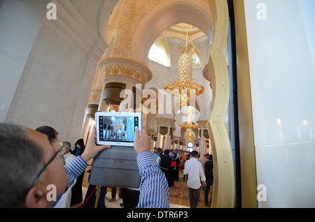 A man using a tablet to take a photo at the Grand Mosque in Abu Dhabi in the United Arab Emirates. Stock Photo