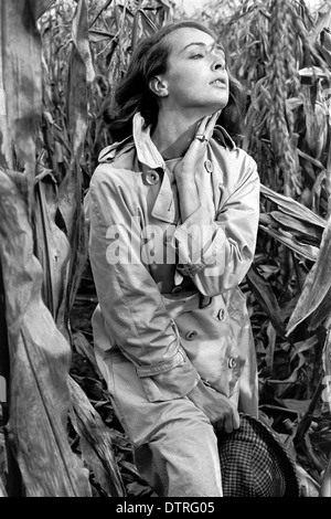 Sixties fashion model with raincoat posing in a maize field