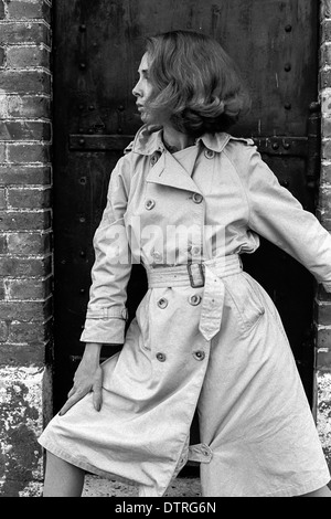 Sixties fashion model with raincoat posing against a black door Stock Photo