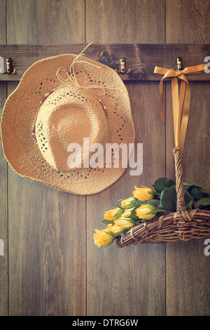 Straw hat and basket of roses hanging on wooden door Stock Photo