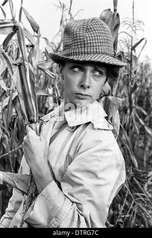 Sixties fashion model with raincoat and hat posing in a maize field