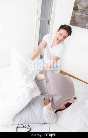 happy boy in pajamas hitting cute girl with pillow Stock Photo