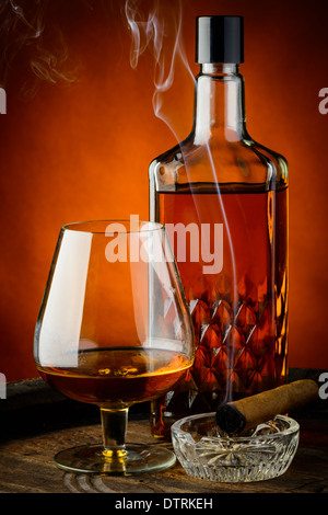 still life with glass and bottle of brandy and smoking cigar Stock Photo