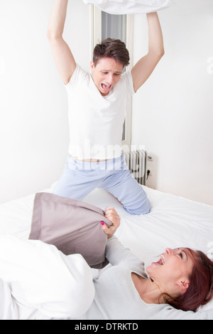 handsome boy in pajamas hitting girl with pillow Stock Photo
