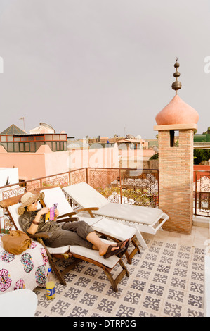A woman reading a book on a roof terrace of Hotel du Tresor, a riad in Marrakesh, Morocco. Stock Photo