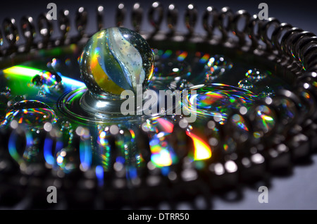 A marble sitting on a CD disc with water droplets and surrounded by curtain rail end hooks Stock Photo