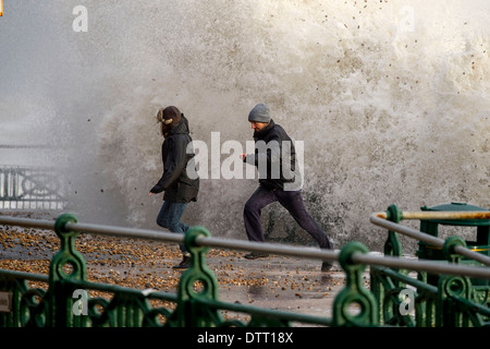 A man runs from huge waves during tidal surges on British coastlines in extreme weather. Scene in Brighton, Sussex, UK