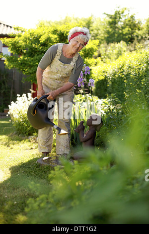 Image of healthy senior woman watering plants with a can in backyard garden. Stock Photo