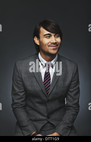 Portrait of handsome young businessman looking away smiling. Attractive male model in suit against black background. Stock Photo