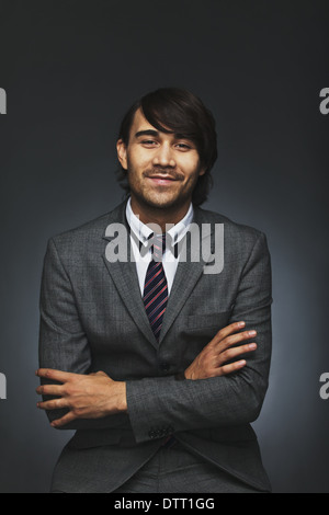 Portrait of positive young man wearing suit sitting with his arms crossed against black background. Handsome businessman. Stock Photo