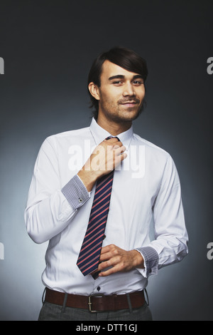 Smart young businessman adjusting his necktie looking at camera smiling. Mixed race male model getting ready for office. Stock Photo