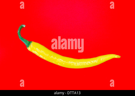 Single yellow spanish pepper against red background Stock Photo