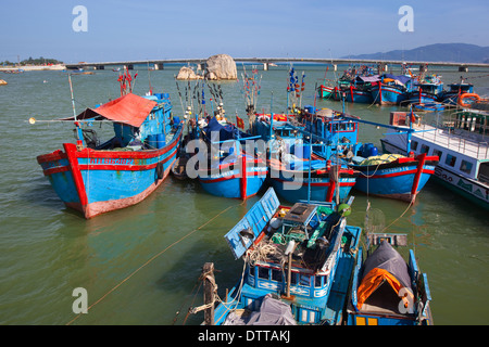 Pretty blue fishing boats moored in the bay with main coastal road bridge beyond at Nha Trang, Khanh Hoa province, Vietnam Stock Photo