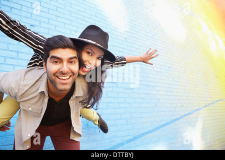 Indian couple piggybacking along brick wall Stock Photo