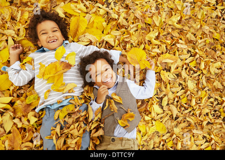 Mixed race boys laying in yellow autumn leaves Stock Photo
