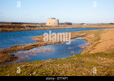 Martello tower standing by coastal defence embankment and lagoon of water, Alderton, Suffolk, England