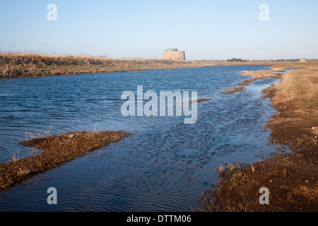 Martello tower standing by coastal defence embankment and lagoon of water, Alderton, Suffolk, England