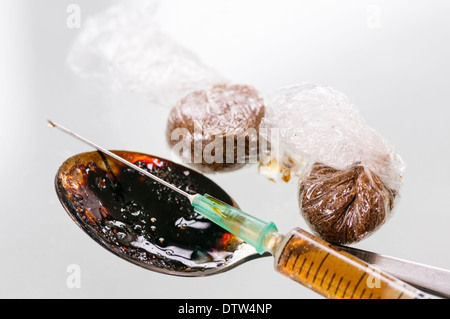 Two wraps of brown drugs, probably heroin, with a dirty spoon and a prepared syringe Stock Photo