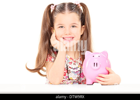 Little girl sitting at a table and holding piggybank Stock Photo