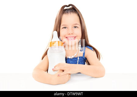 Stylish little girl holding a huge baby bottle seated at table Stock Photo