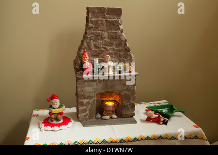 An assortment of Christmas decorations around a miniature stone fireplace, including a vintage Santa bobble-head on the mantle. Stock Photo