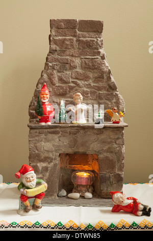 An assortment of Christmas decorations around a miniature stone fireplace, including a vintage Santa bobble-head on the mantle. Stock Photo