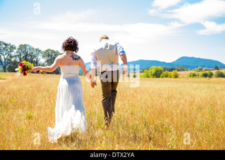 Bride and groom walking together on their wedding day through a field in Oregon. Stock Photo