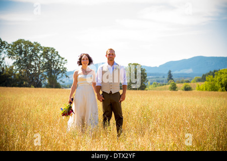 Bride and groom standing together in a field on their wedding day. Stock Photo