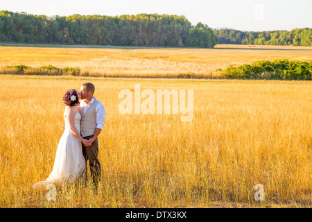 Wedding couple shares a romantic moment in a field or meadow at sunset on their wedding day. Stock Photo