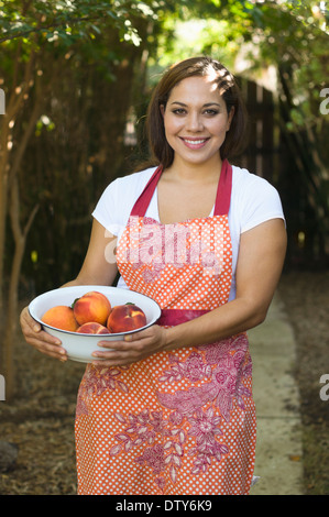Mixed race woman holding bowl of peaches outdoors