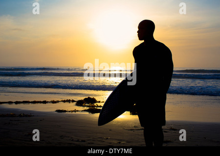 Silhouette of mixed race man holding surfboard on beach Stock Photo