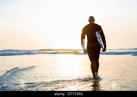 Mixed race man walking with surfboard on beach Stock Photo