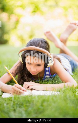Mixed race girl listening to headphones and drawing outdoors Stock Photo